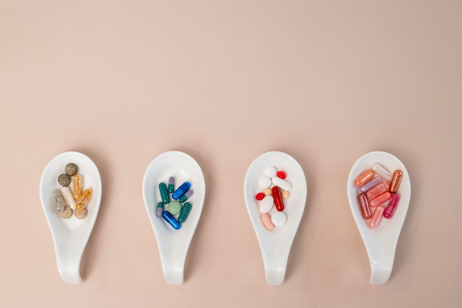 Four white ceramic spoons in a row, each holding a different set of capsules and tablets.