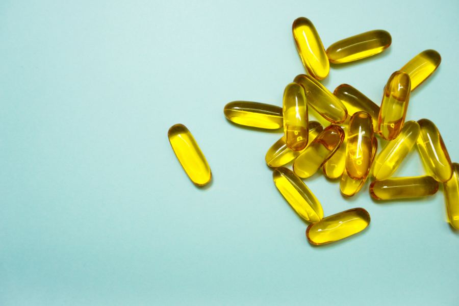 Amber softgels scattered across a pale blue-green surface.