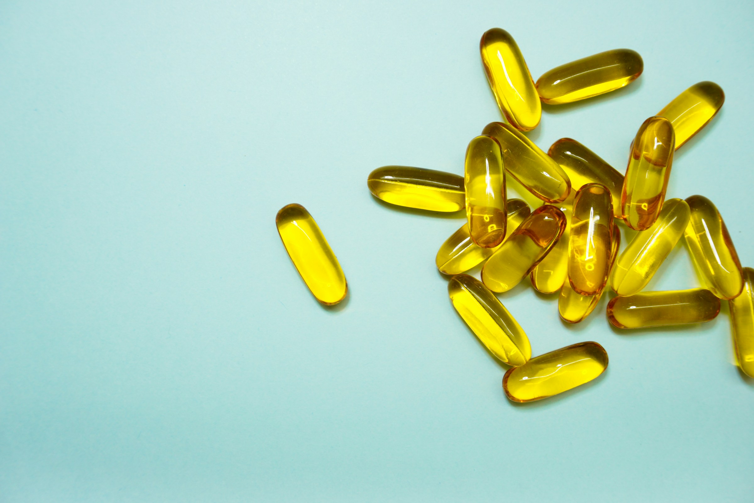 Amber softgels scattered across a pale blue-green surface.